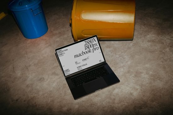Laptop mockup on floor with open display showing screen resolution, near yellow object and blue container, for graphic designers and templates.