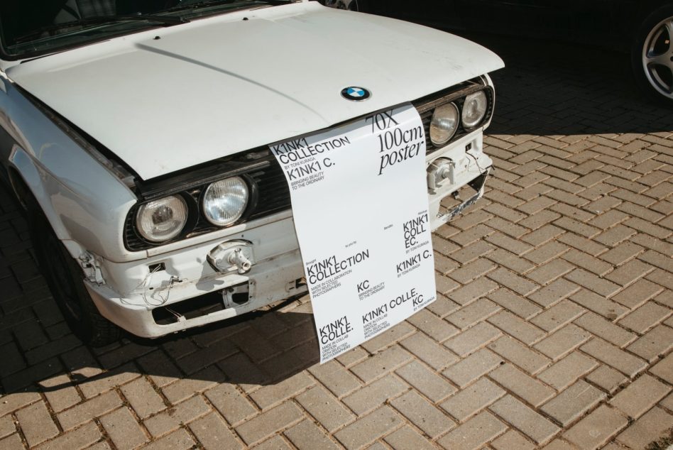 White K1NK1 poster on vintage BMW hood with brick pavement backdrop