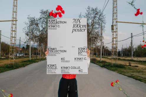 Person holding large poster mockup in a natural outdoor setting, showcasing clear space for design presentation, framed by greenery.