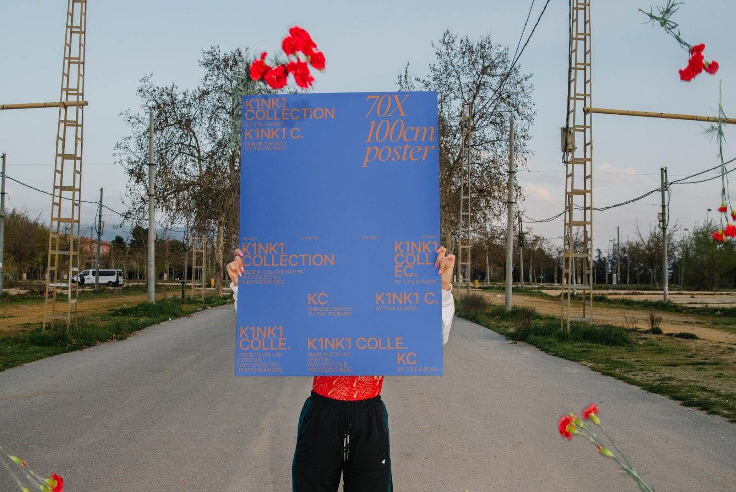 Person holding large blue poster mockup with text for design display in an outdoor setting with foliage and power lines in the background.