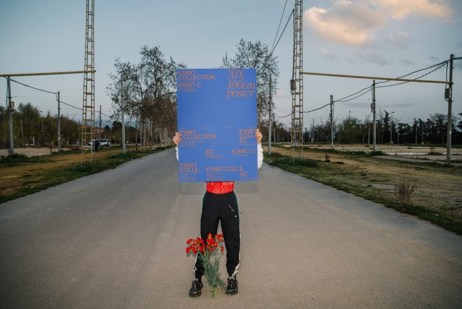 Person holding blue poster mockup in natural outdoor setting with clear space for design presentations, ideal for graphic designers.