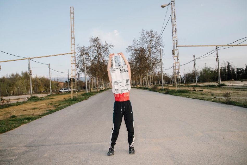 Person with obscured face holding a tote bag on head on a deserted road, ideal for mockup graphics design showcasing urban streetwear.