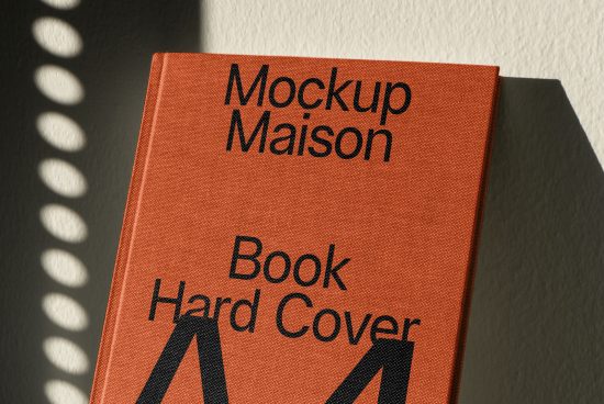 Orange hardcover book mockup with typographic design on cover casting a crescent shadow, ideal for book design presentations.