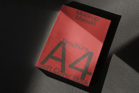 Red A4 brochure mockup lying on a textured surface with dramatic shadows, realistic soft cover book design, perfect for presentations and portfolios.