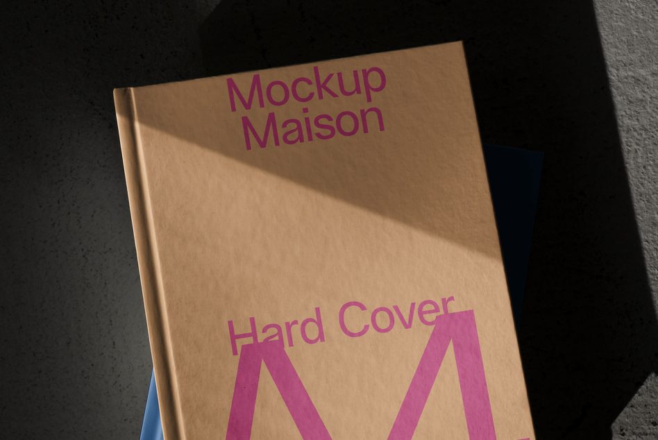 Tan hardcover A4 book with magenta letters on concrete background with light