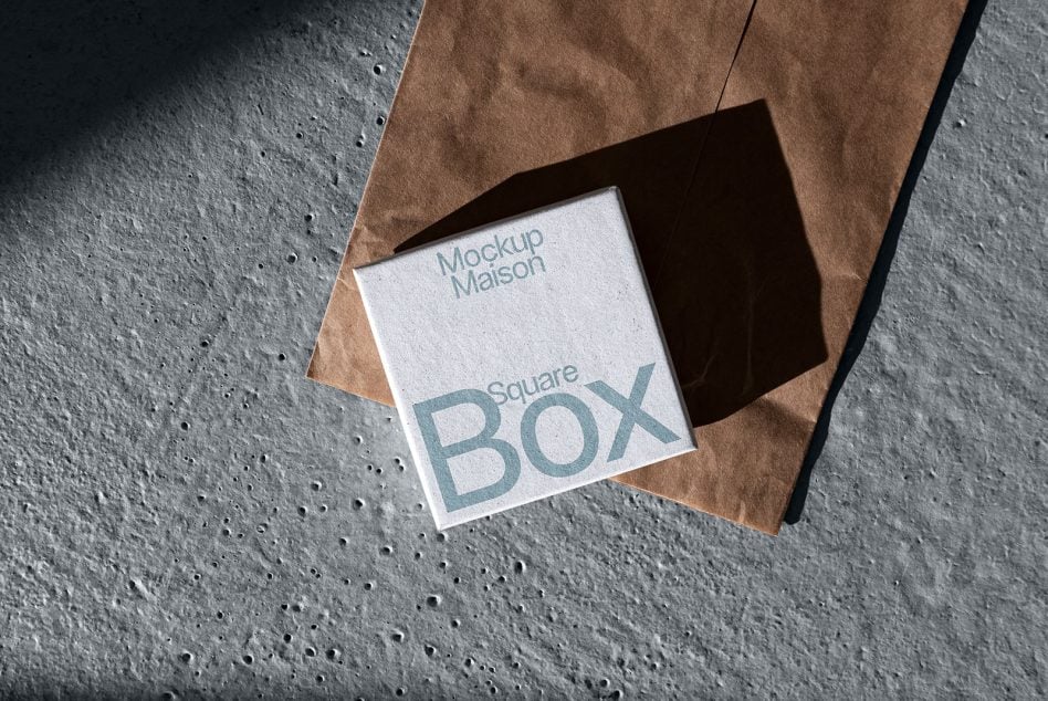 Square box mockup nested in kraft paper envelope on concrete surface