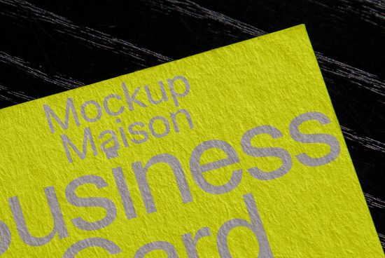 Close-up view of a vivid yellow business card mockup with embossed grey text on a dark textured background, ideal for branding and stationery design.