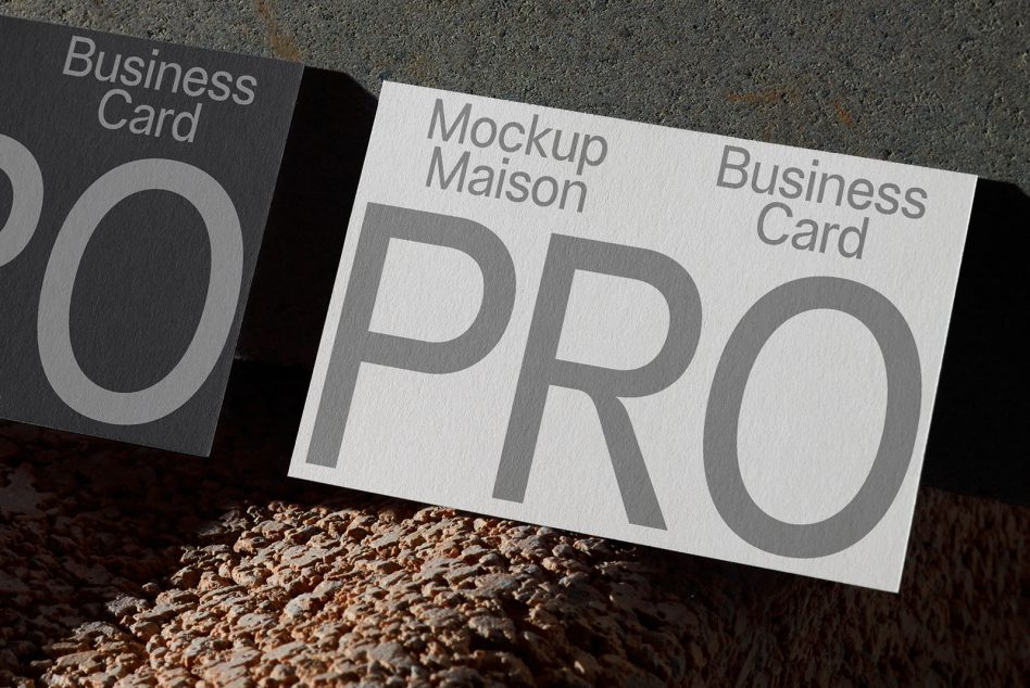 Black card next to white business card mockup on textured ground showing PRO