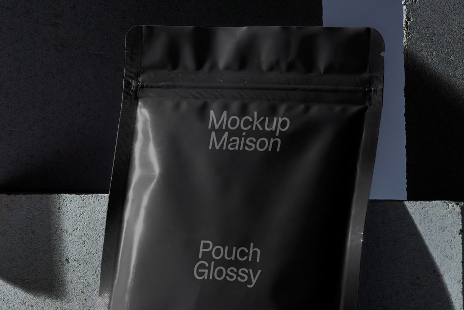 Black glossy stand-up pouch mockup for product packaging design against a textured background with distinctive shadows.