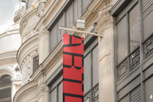 Red banner mockup hanging from a classic building facade, perfect for displaying design templates and graphics for urban outdoor advertising.