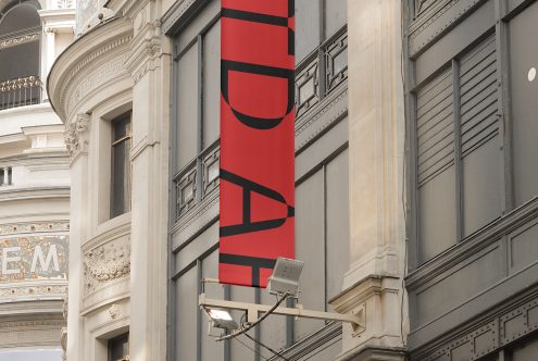 Red urban banner mockup hanging on a classic building, with clear space for designers to showcase branding graphics and logos.