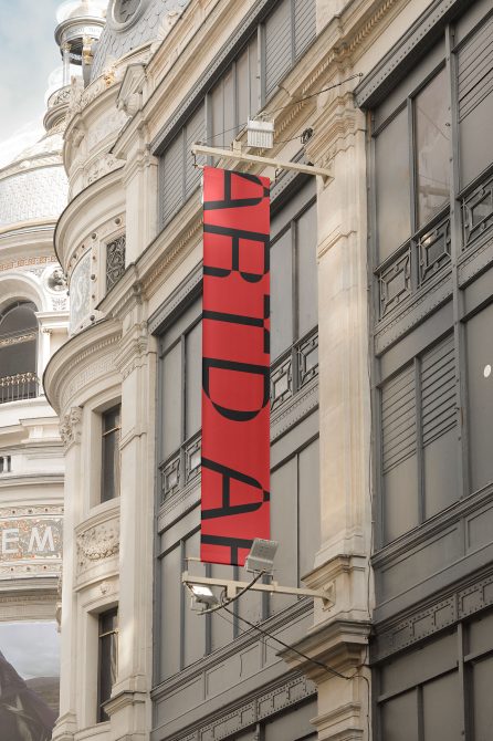 Red vertical banner mockup hanging on classic building exterior for outdoor advertising with clear space for custom design.