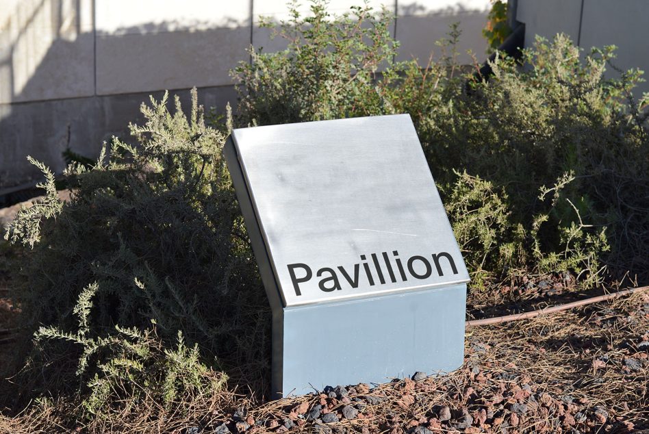White cubic kiosk with Pavillion text surrounded by desert plants