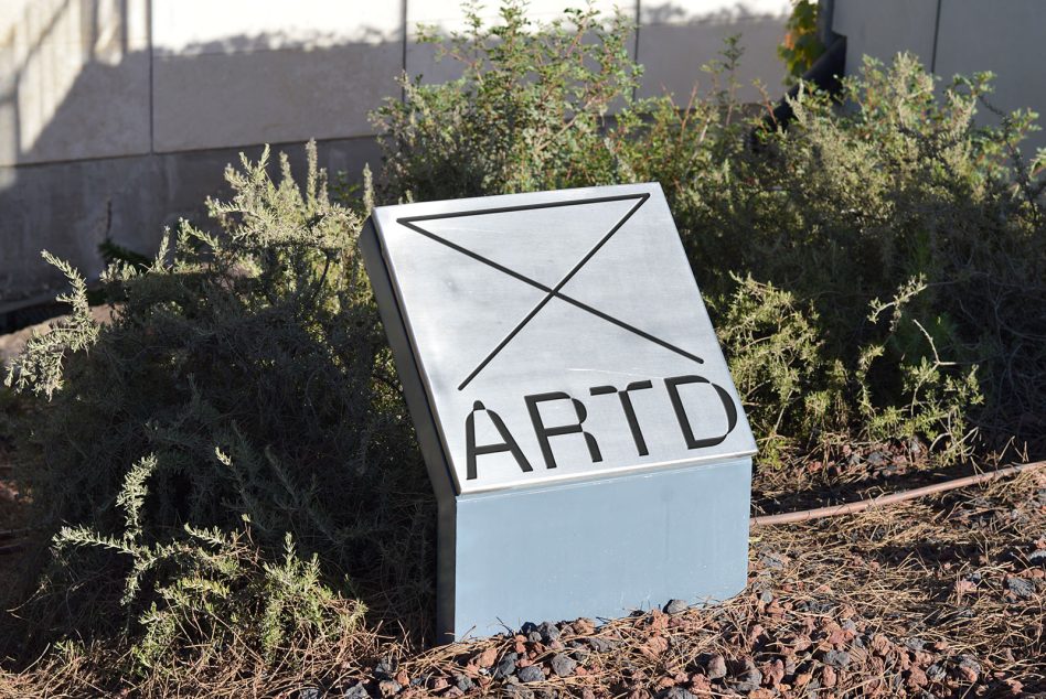 White wayfinding sign with hand-drawn envelope icon, black text reads ARTD