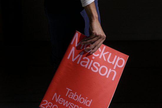 Person holding a red tabloid-sized mockup with bold typography design ideal for presenting editorial and graphic designs on a marketplace.