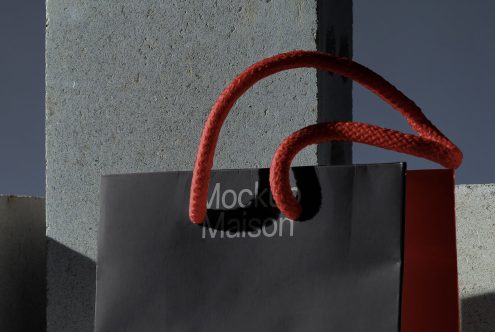 Elegant shopping bag mockup with red handles against a minimalist architectural background, ideal for showcasing branding designs.