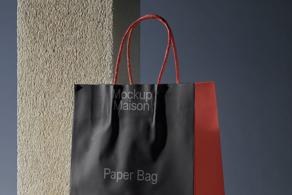 Black tote bag with red handles displayed against cream textured wall surface