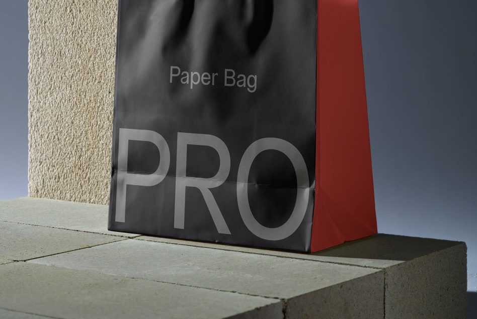Black paper bag with red side gusset sitting on concrete next to textured wall
