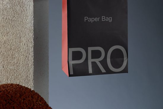 Elegant black paper bag mockup hanging on wall with contrasting red handle, realistic shadow, clear sky background perfect for packaging design display.