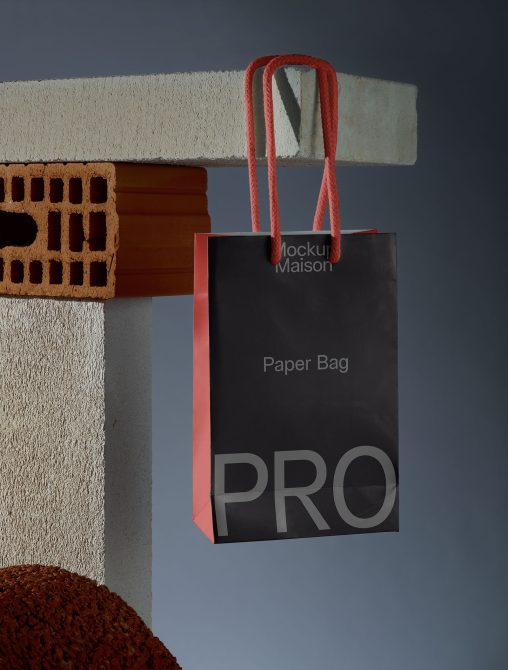 Black paper bag mockup with red handles hanging against a textured background, suitable for product packaging designs.