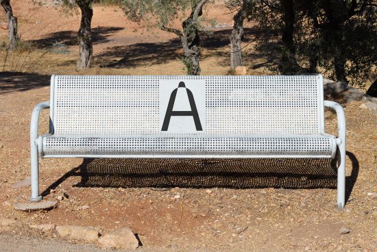 White outdoor bench with a black letter A design in park setting ideal for font and graphic design mockup presentations.