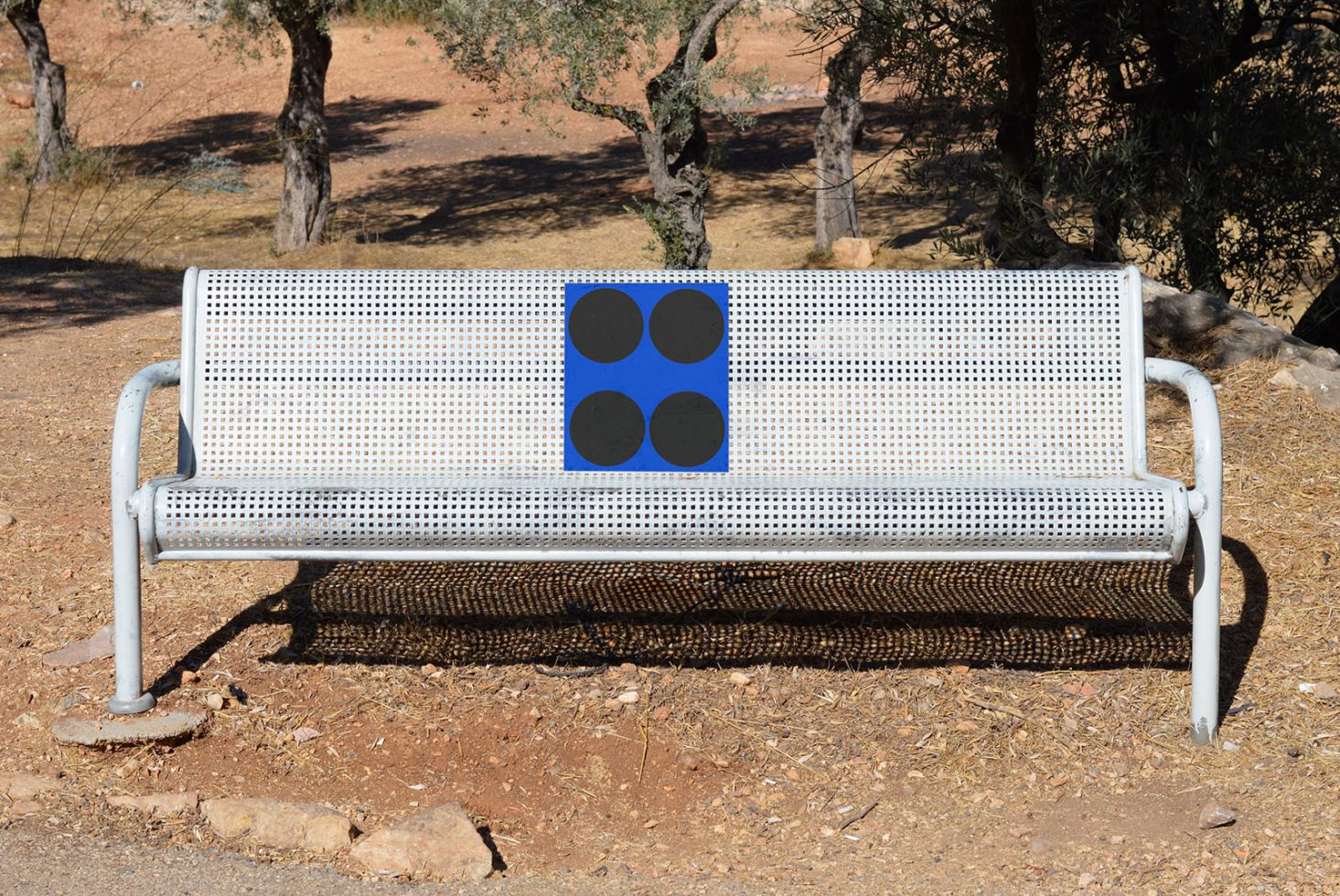 White perforated metal bench in an outdoor setting with trees in the background for mockups and design presentations.