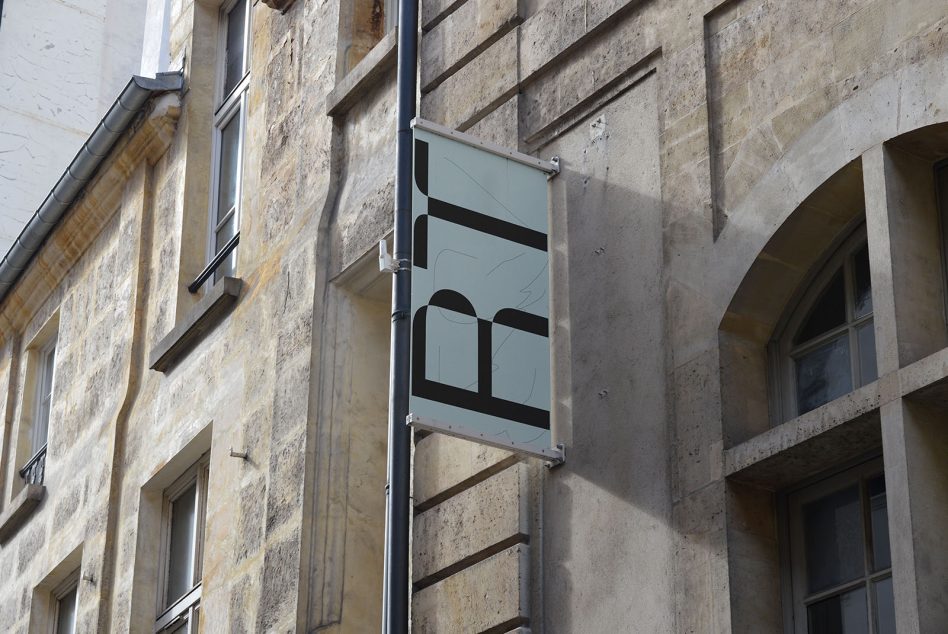 Vertical banner mockup on an old building wall, displaying stylized letter graphics, clear sky, urban outdoor advertising setting for designers.