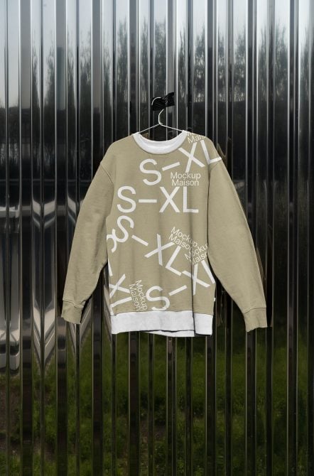 Tan crewneck sweatshirt hanging on industrial metal fence backdrop