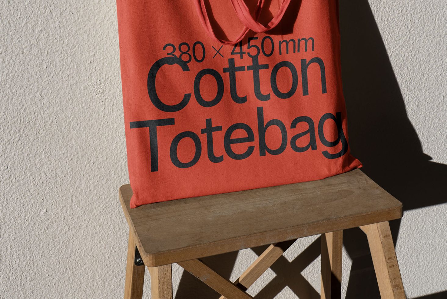 Red cotton tote bag mockup on wooden stool with shadow, clean design, high-resolution fabric texture, graphic design asset.