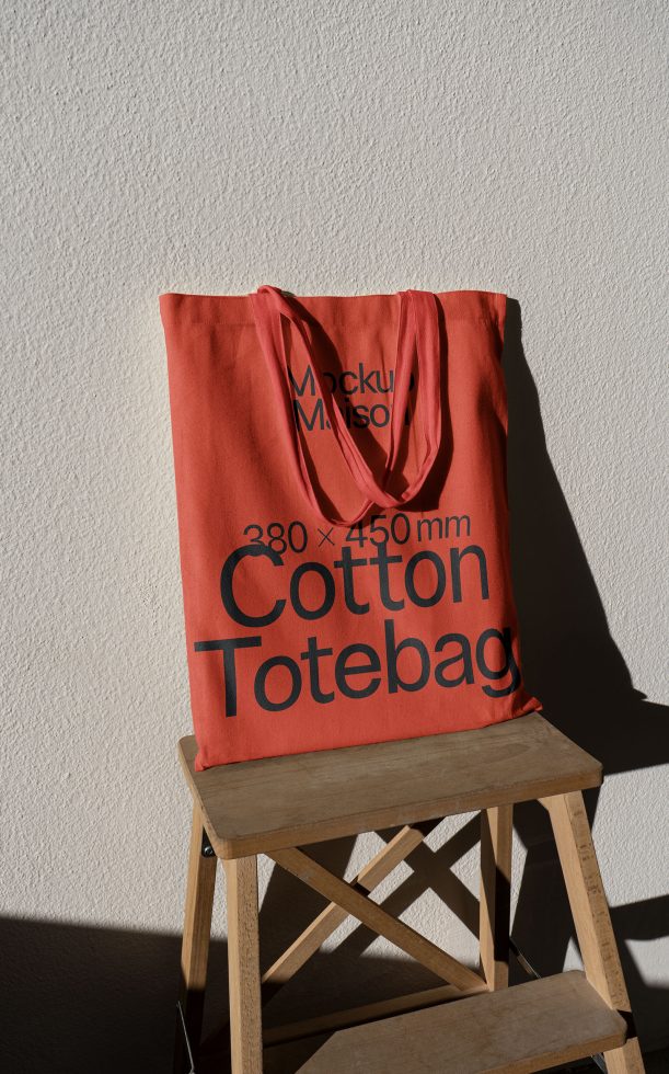 Red cotton tote bag mockup on wooden stool with shadow, realistic texture, for design presentation, eco-friendly bag template.