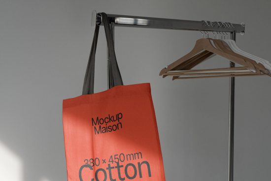 Red tote bag mockup hanging on metal stand beside wooden hangers, showcasing customizable design surface for branding.