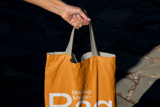 Person holding an orange tote bag mockup with customizable design area, showcasing design space for branding and advertising.