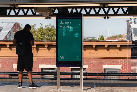Man standing at train station next to digital screen mockup, cityscape background, urban advertising display, outdoor signage template.