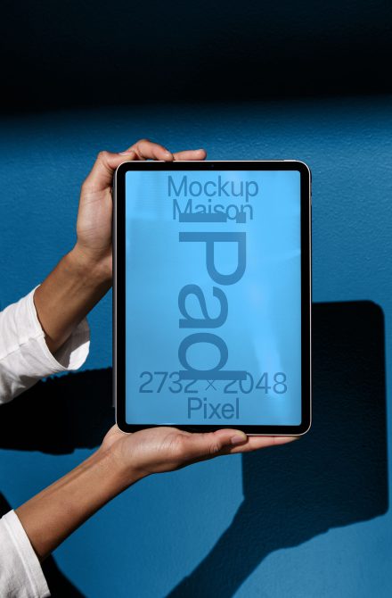 Hands holding tablet portrait mode with blue screen on blue background