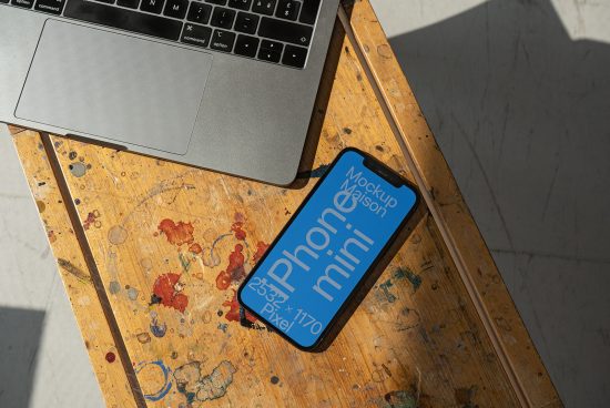 Laptop and smartphone mockup on a wooden table with artistic paint splatters, showcasing a phone screen design, ideal for designers and digital assets.