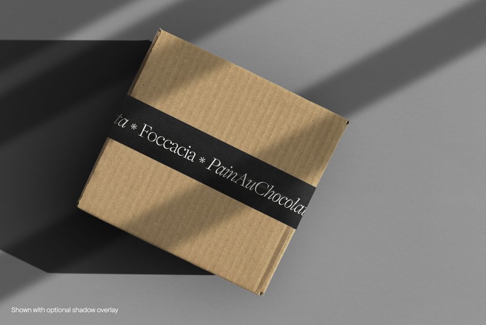 Cardboard box mockup with elegant typography on black tape, realistic shadow overlay, ideal for branding and packaging designs.