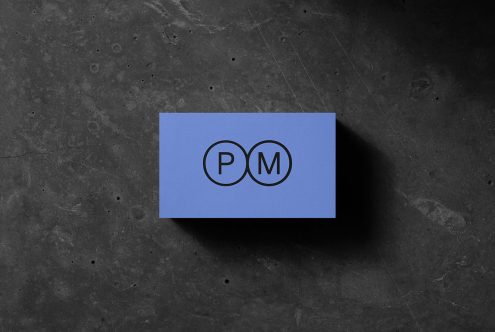 Business card mockup with PM initials lying on a textured dark stone surface, perfect for presenting branding designs.