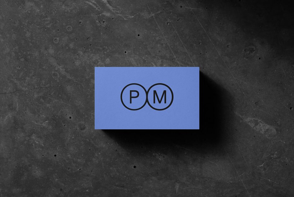 Blue business card with PM logo in two connected circles on dark concrete background
