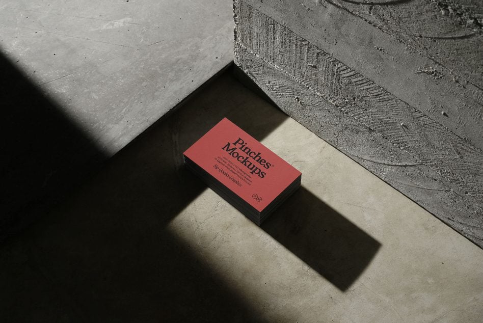 Business card mockup with coral front showing text, stacked on concrete with dramatic shadow