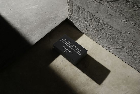 Stack of black business cards on a textured concrete surface, showcasing elegant typography design under dramatic lighting.