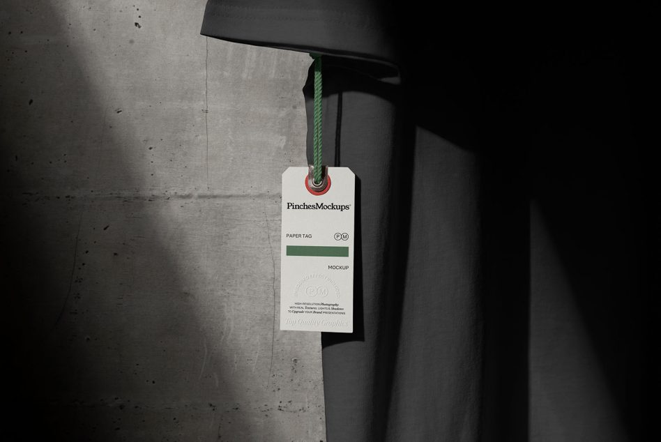 Stylish paper tag mockup with a green rope hanging under a lamp, against a textured wall, perfect for designers to display branding.