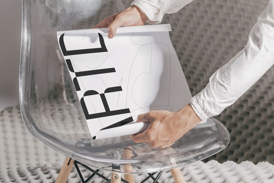 Person unwrapping a bold typographic poster on a modern transparent chair. Ideal for font presentation mockups for designers.