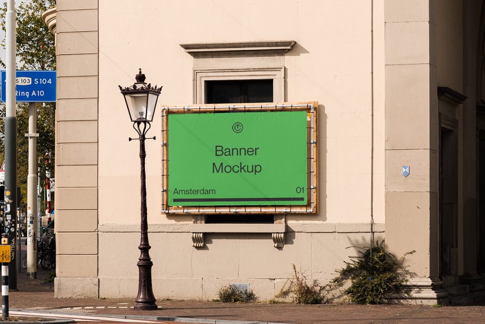 Green banner with white frame mounted on cream building facade, street lamp visible