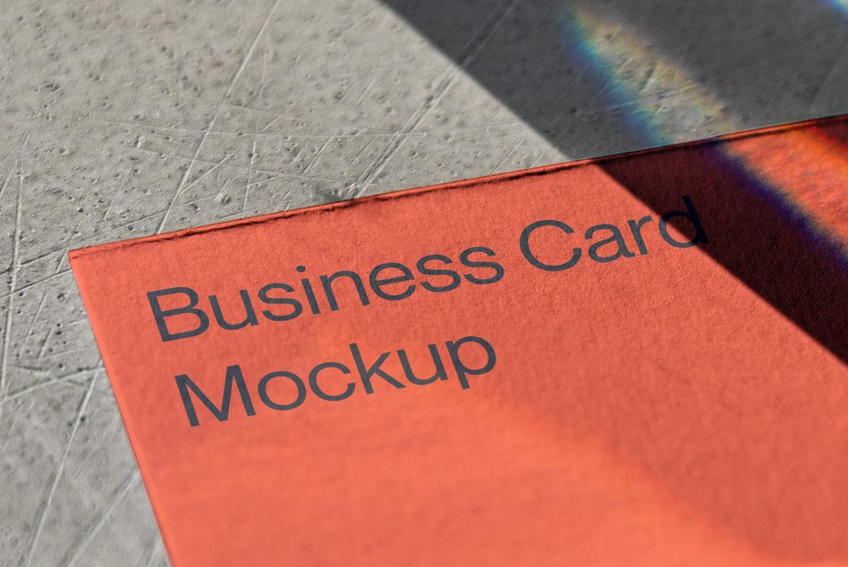 Bright orange business card with dark text on concrete surface with rainbow light