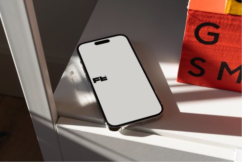 Modern product photography of iPhone on white surface with orange magazine nearby