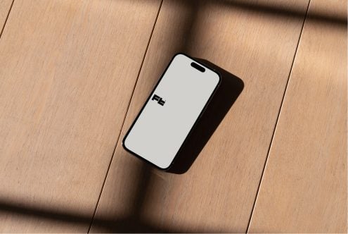 Angled iPhone on wood table with natural light creating dark shadow below device