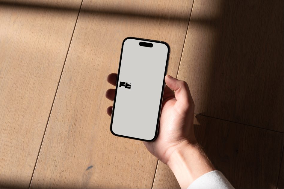 iPhone lying flat on wood flooring showing white display with FE branding visible