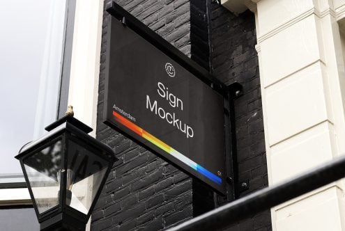 Black hanging sign with rainbow stripe detail on brick storefront wall