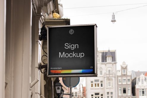 Black storefront sign with rainbow color bar hanging on historic Amsterdam building facade