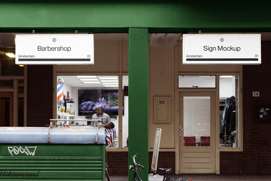 Two white signs above storefronts on green bar storefront divider, barber shop visible inside